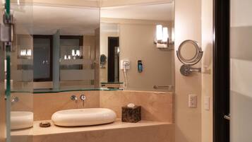 A modern bathroom with a glass-enclosed sink, a marble countertop, a large mirror, and a round mirror on the wall.