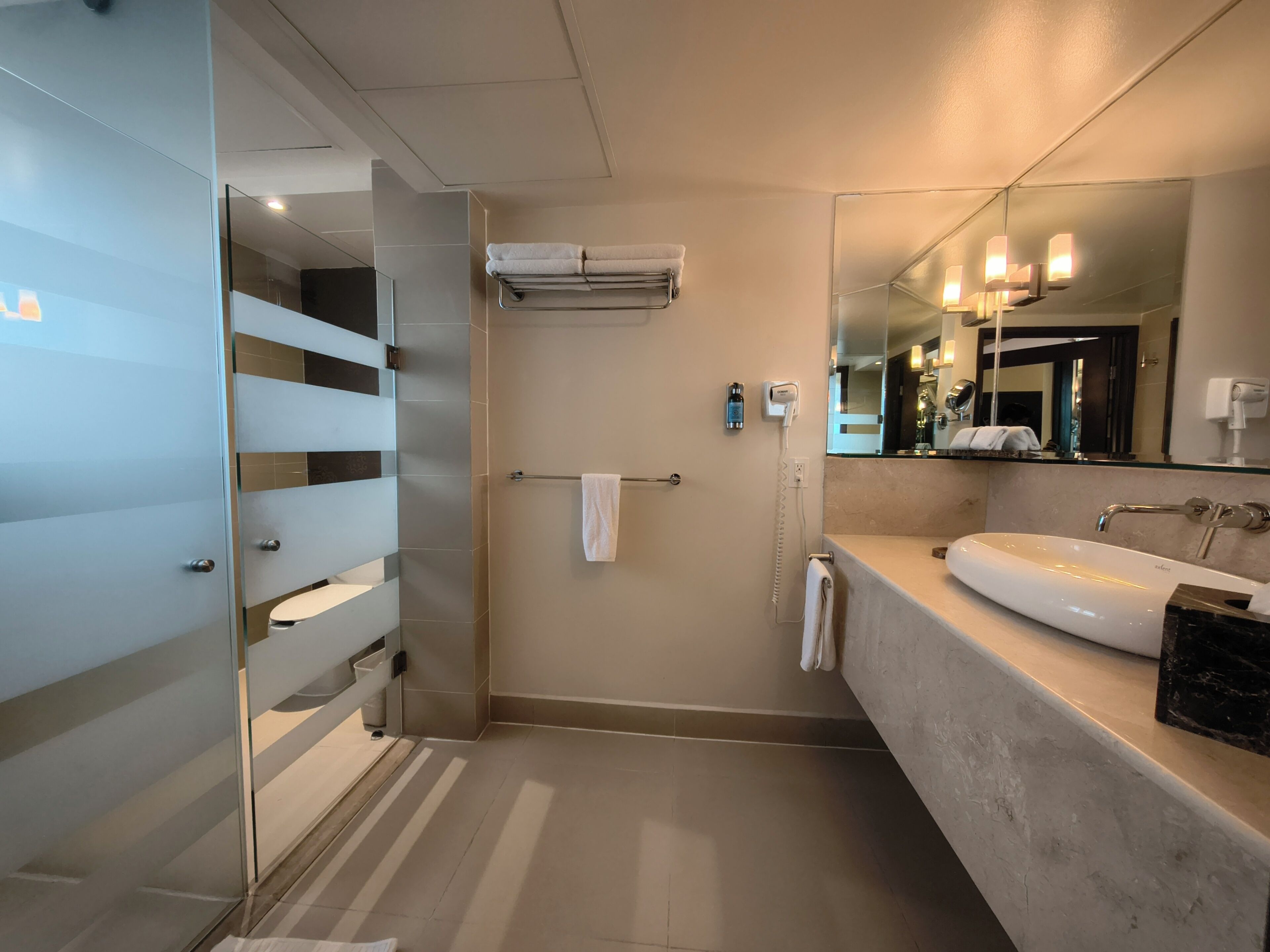 Een moderne badkamer met een douchecabine van glas, een grote spiegel, een witte wasbak en een handdoekrek.
