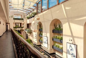 A multi-level atrium with a glass ceiling, indoor plants, and artwork on the walls.