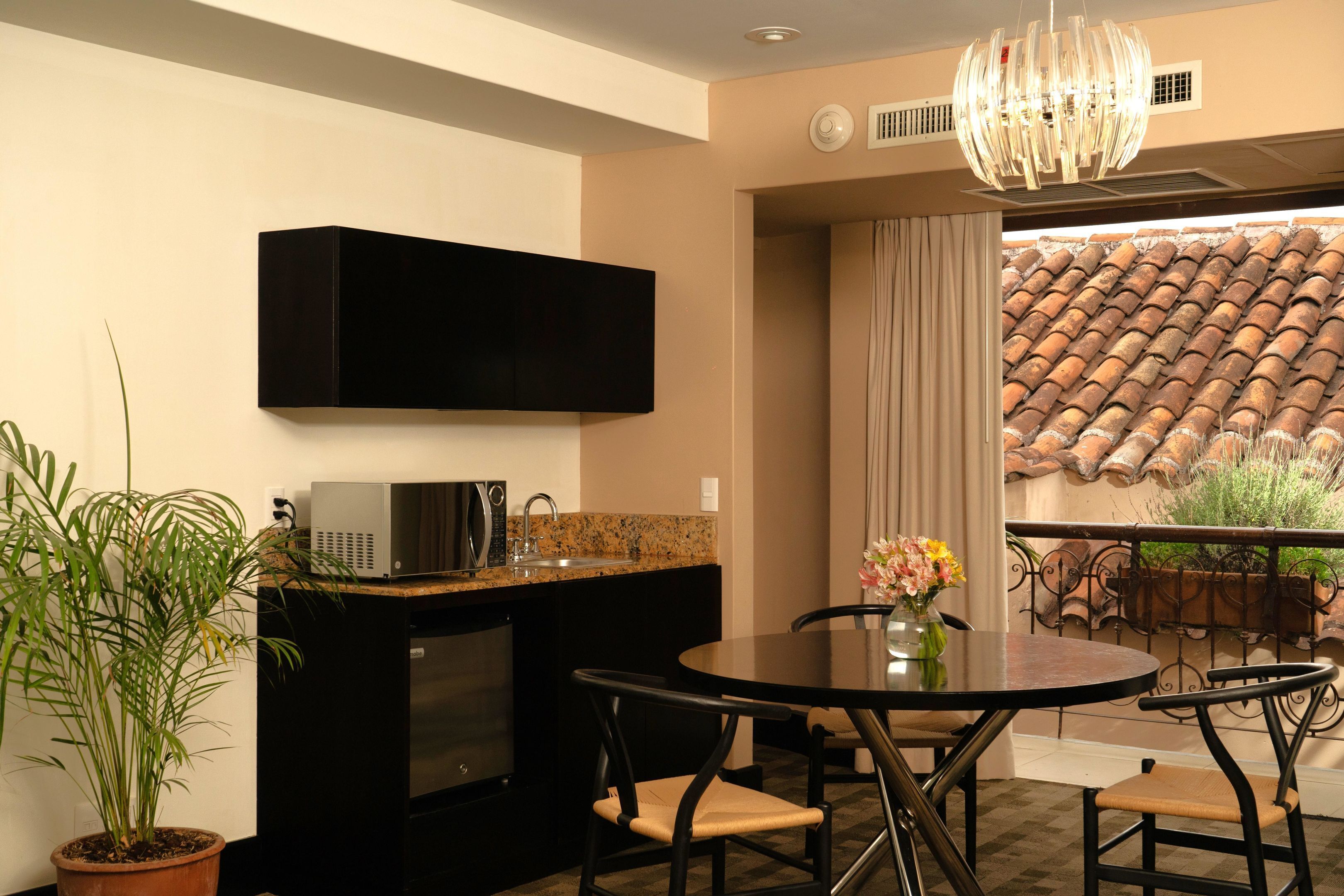 A compact kitchen with a flat-screen TV, a microwave, and a sink. There is a dining table with chairs and a potted plant.