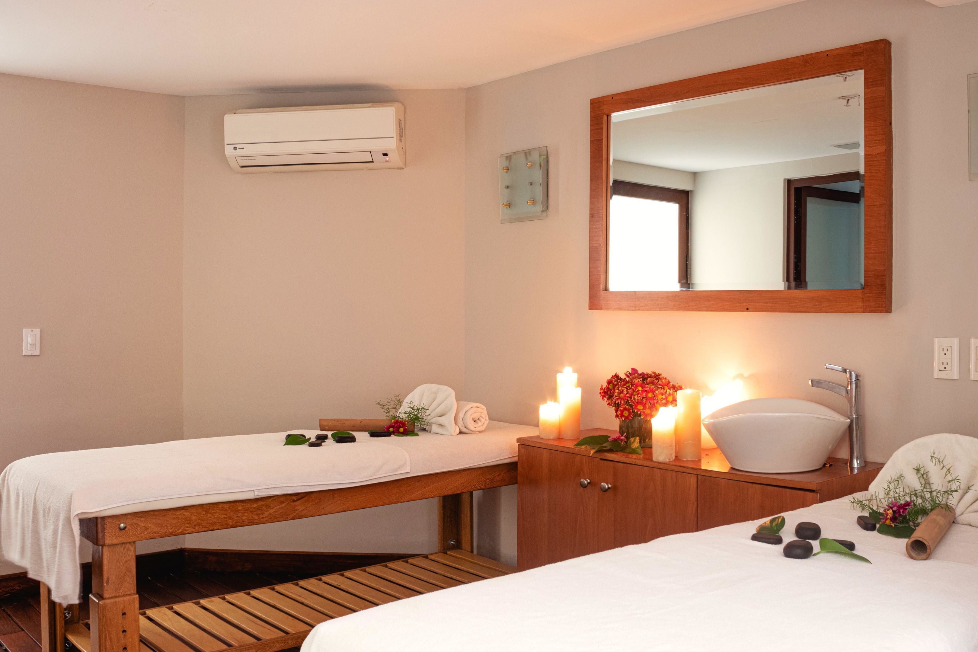 A bedroom with two beds, a wooden bench, a sink, and a mirror.