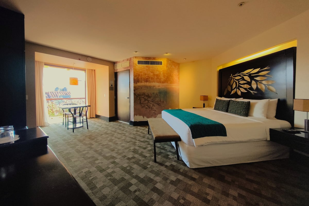 Une chambre d’hôtel comprenant un lit, un bureau, une chaise, un balcon et un mur décoré de motifs végétaux.