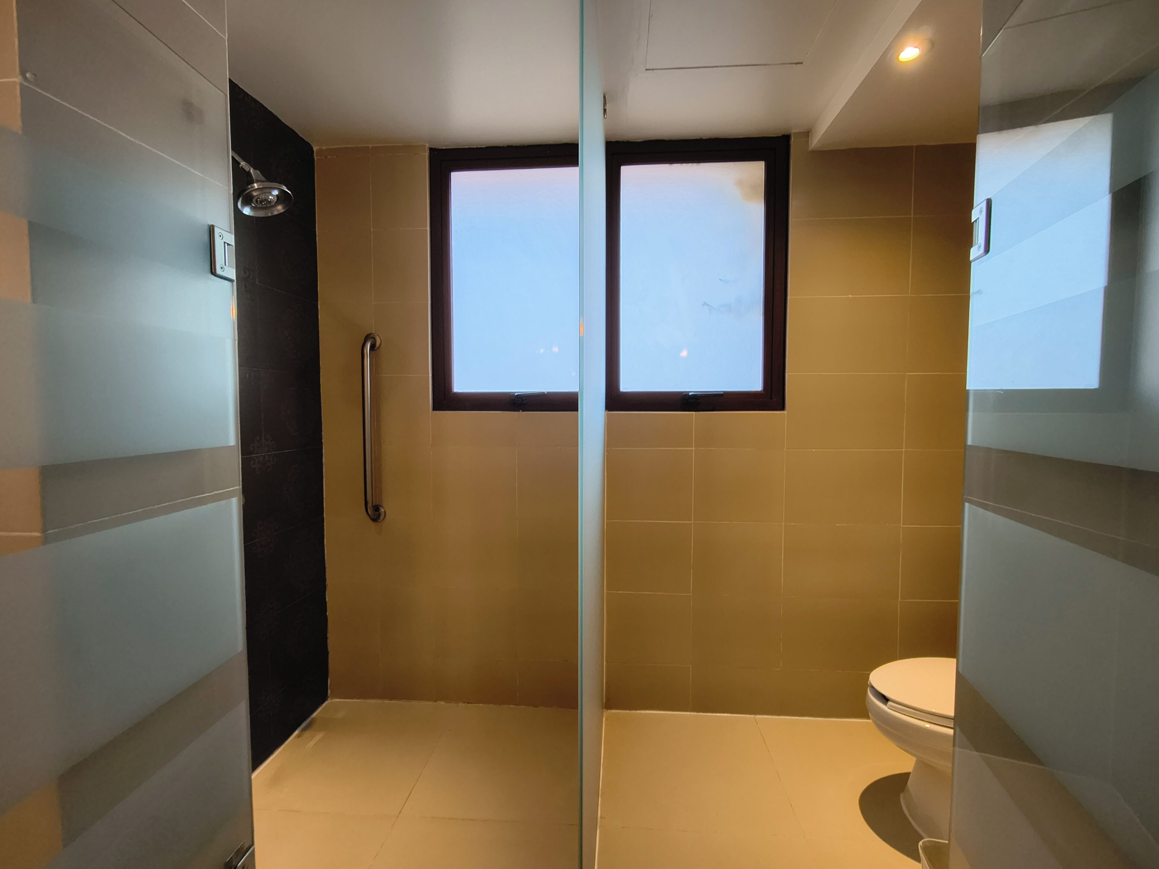 Un baño con separador de vidrio, ventana, inodoro y zona de ducha.