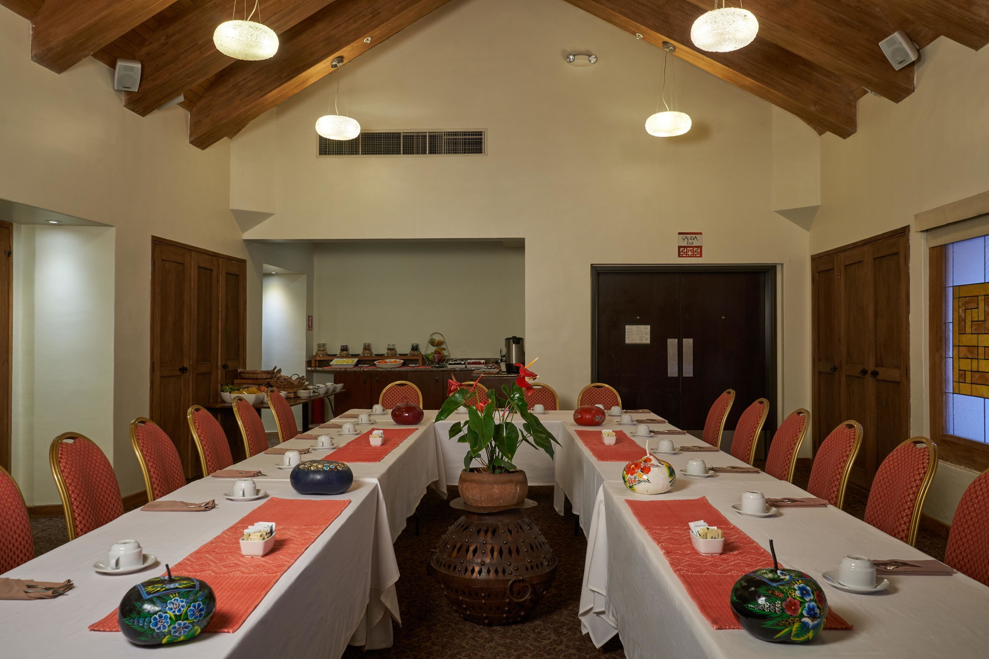 A conference room with long tables, red chairs, and a large decorative pot in the center.
