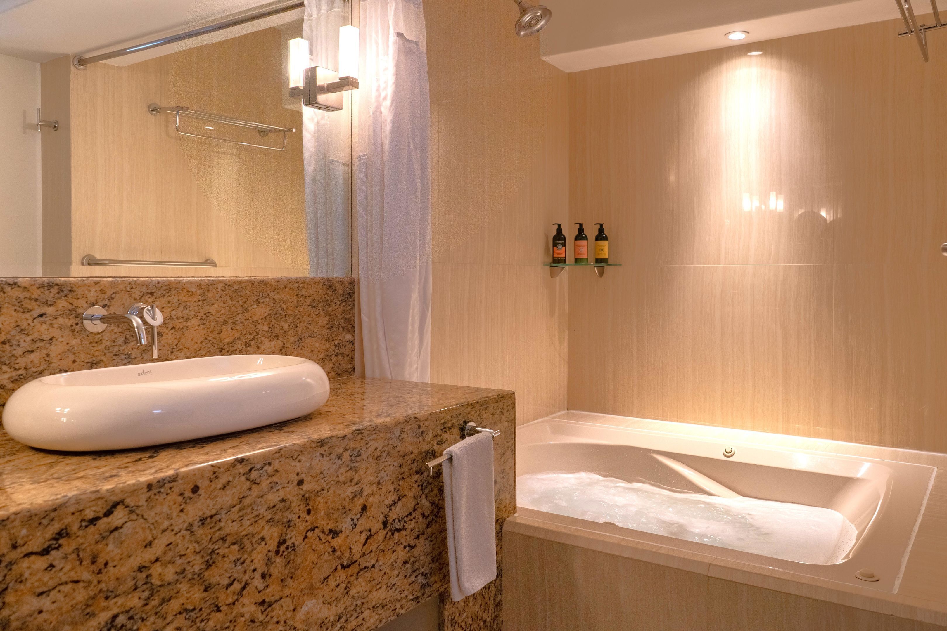 Une salle de bain avec un comptoir en granit, un lavabo blanc et une baignoire.