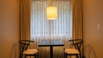 A dining area with a table and two chairs, a hanging lamp, and sheer curtains.