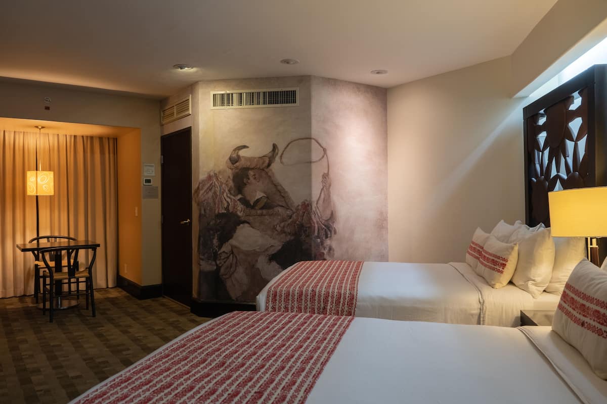 Une chambre d’hôtel avec deux lits, une table à manger et une fresque représentant un taureau sur le mur.