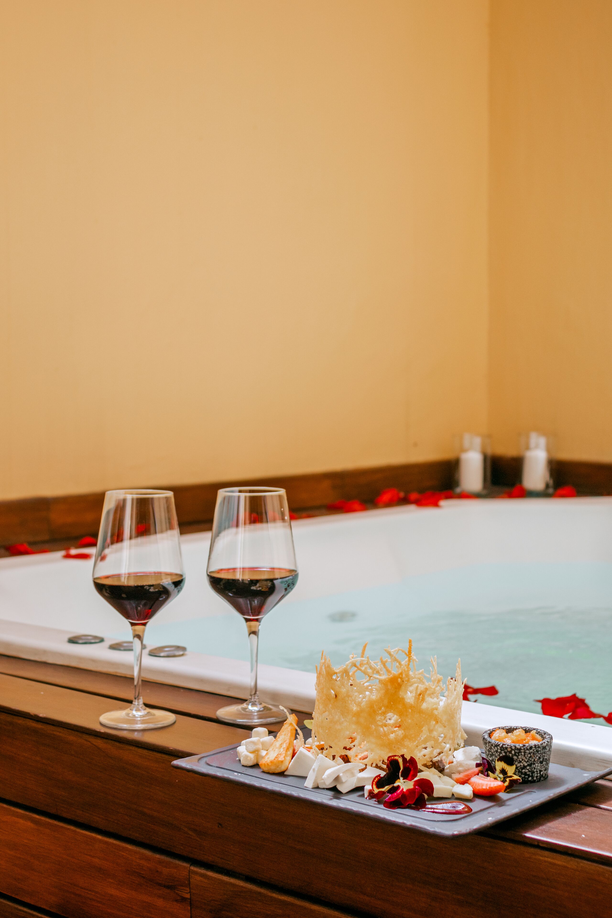 A spa setting with a bathtub, two glasses of red wine, and a tray with food and a decorative item.
