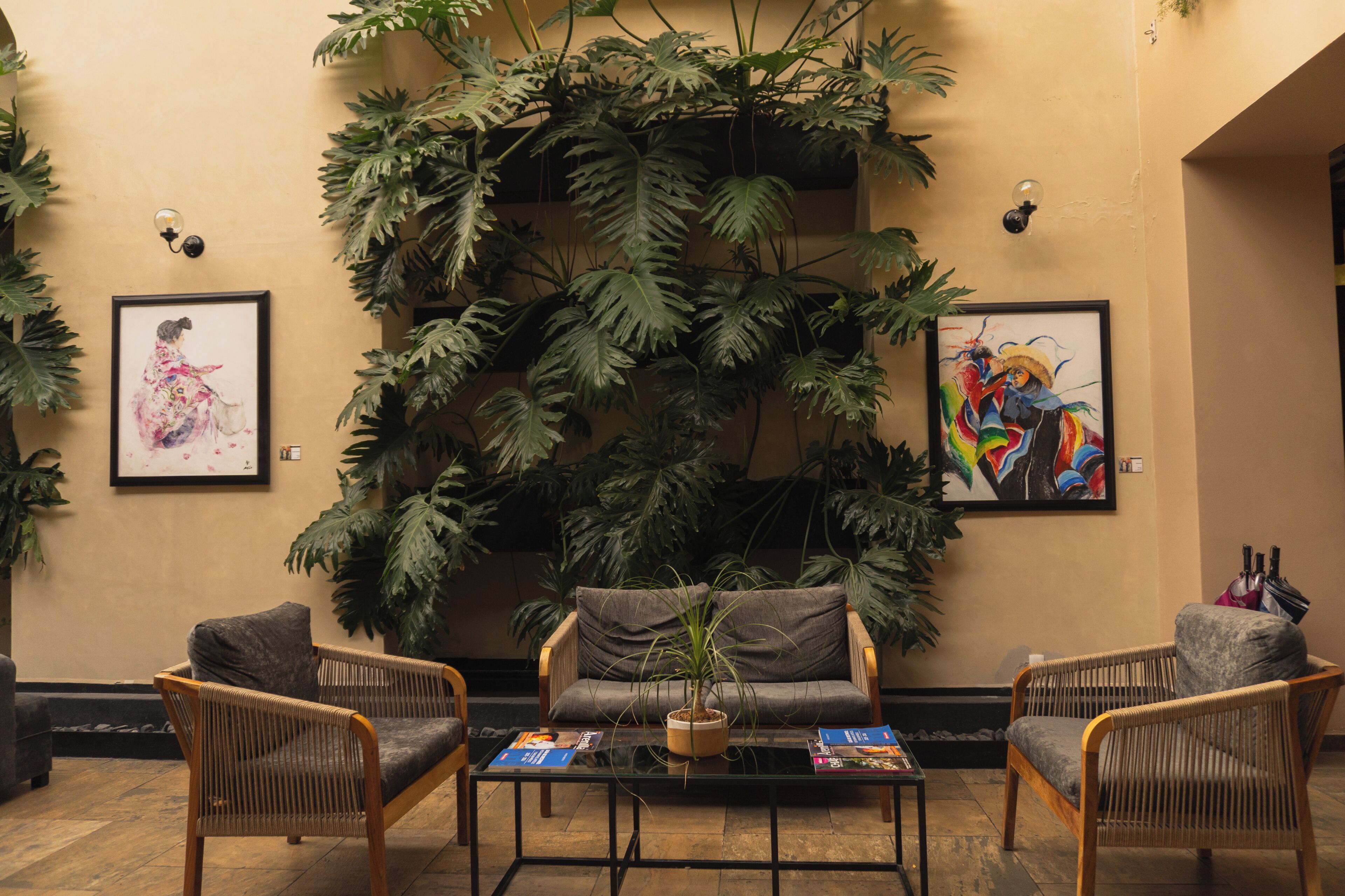 Un vestíbulo con una gran planta de interior, dos obras de arte enmarcadas y una zona de estar con sillas de mimbre y una mesa de centro.