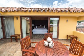 A hotel room with a bed, a wooden table with chairs, and a balcony with a tiled roof.