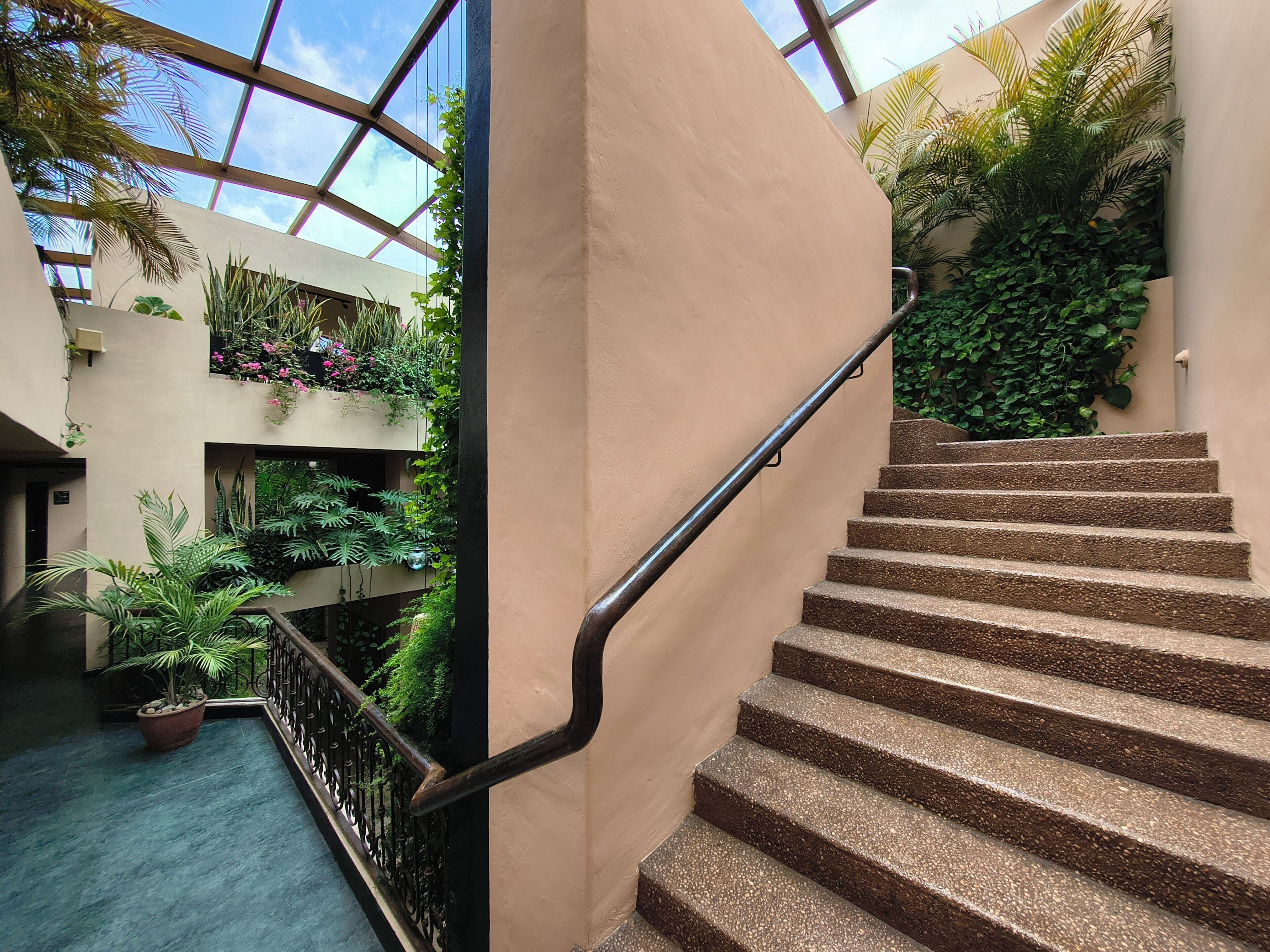 A multi-level indoor space with a staircase, greenery, and a glass ceiling.