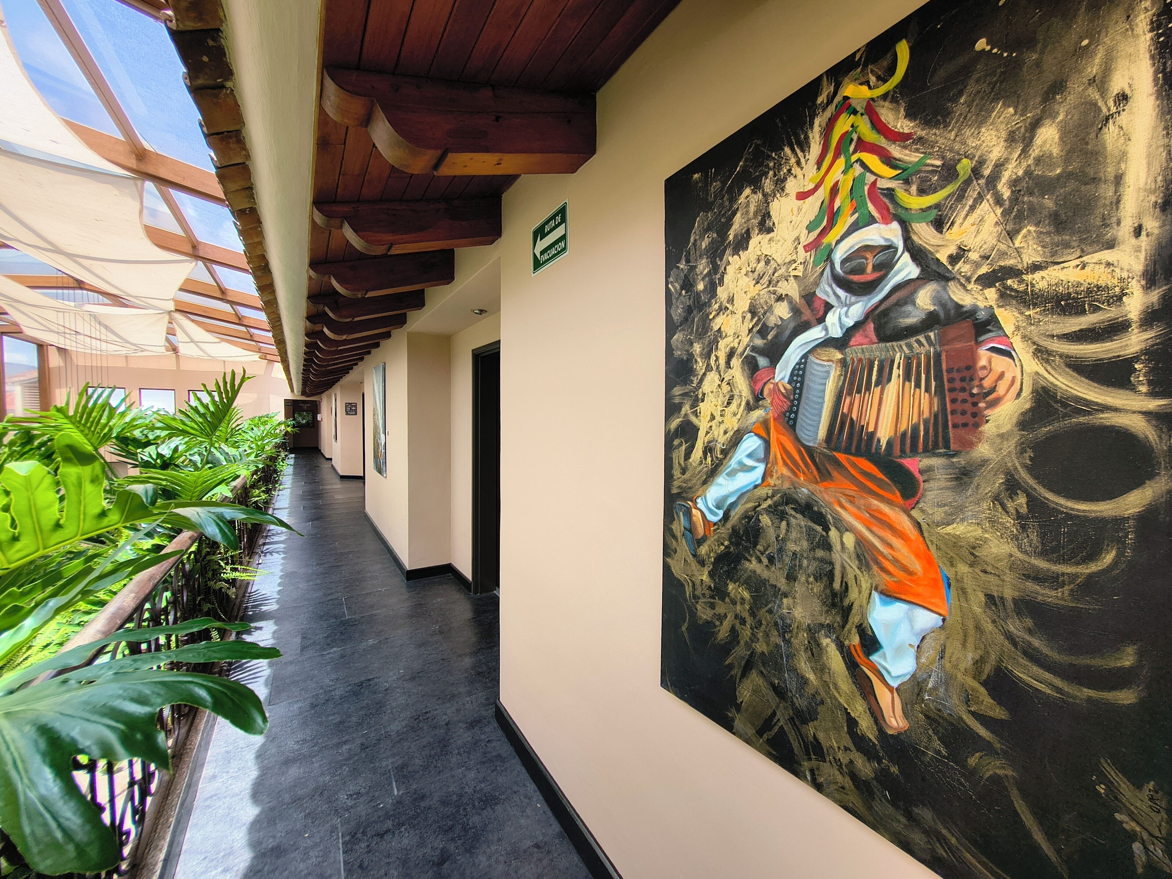 A corridor with a large abstract painting, wooden ceiling beams, and potted plants.