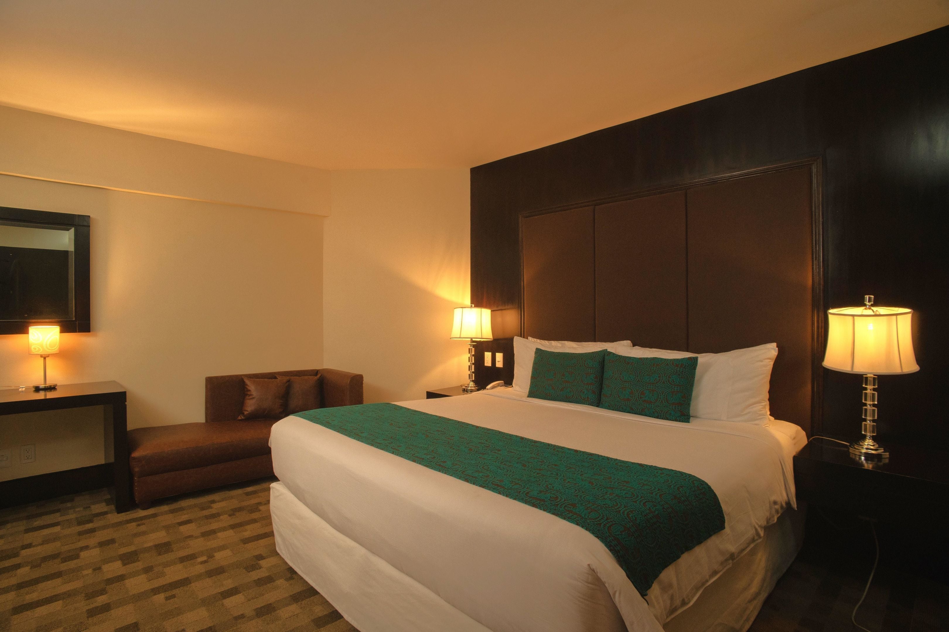 Een hotelkamer met een groot bed, twee bedlampen, een kleine bank en een nachtkastje.