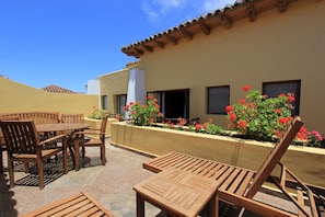 An outdoor patio with wooden furniture, a tiled floor, and a building with a tiled roof and windows.