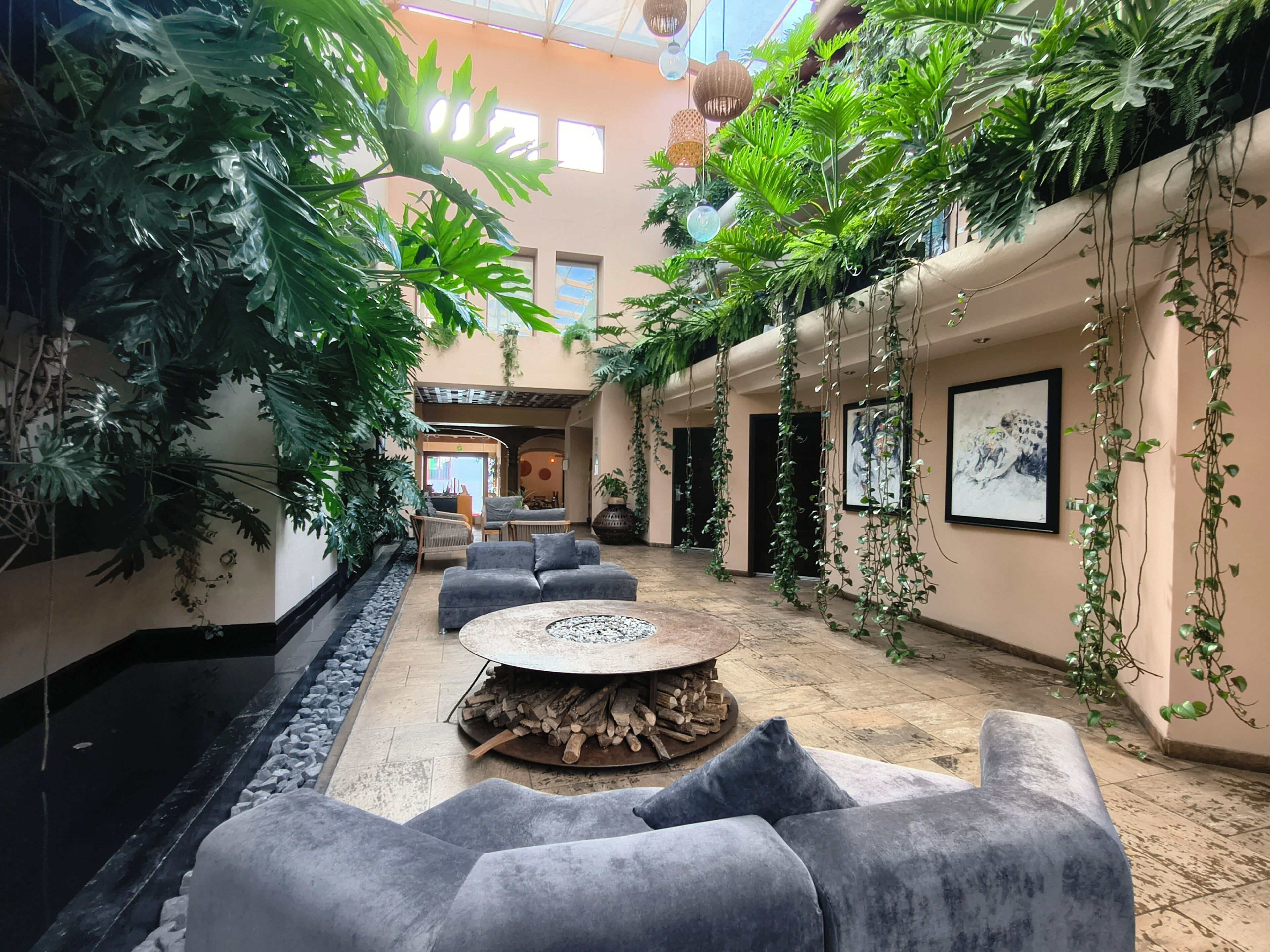 An indoor space with a central seating area, a fire pit, and lush greenery.