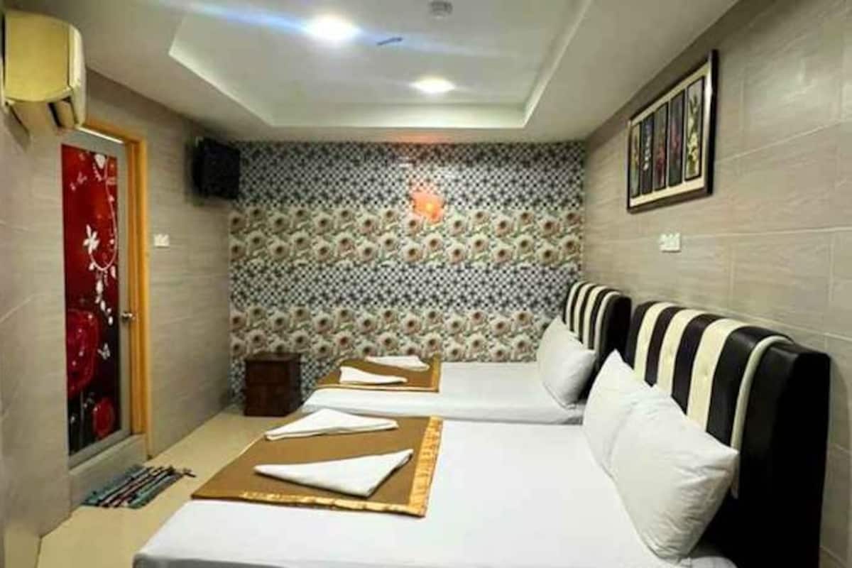 A hotel room with two beds, a red door, patterned wallpaper, and a framed picture on the wall.