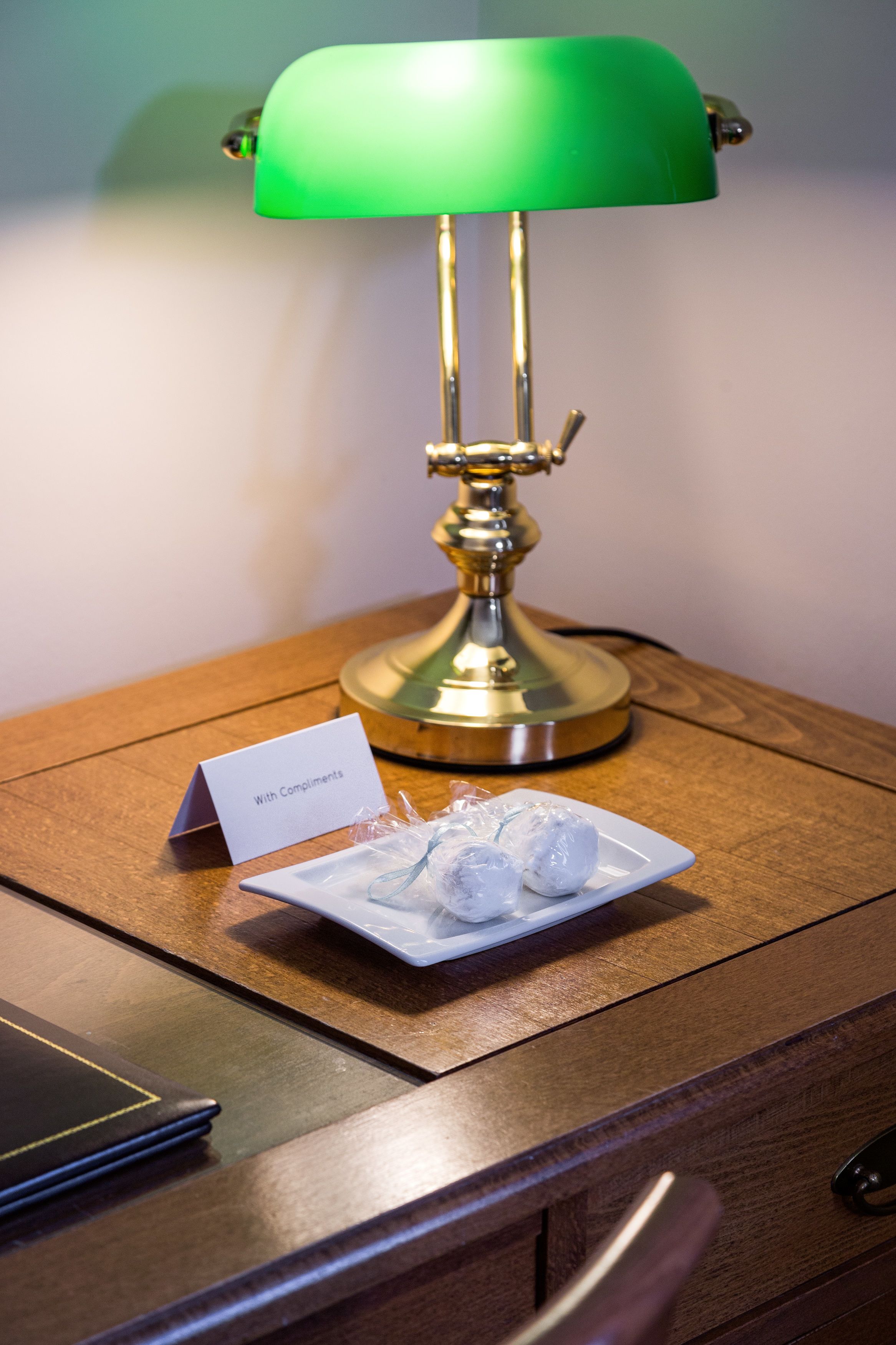 Une lampe de bureau verte est posée sur une table de chevet en bois, à côté d’un porte-nom et d’une assiette remplie de glaçons.