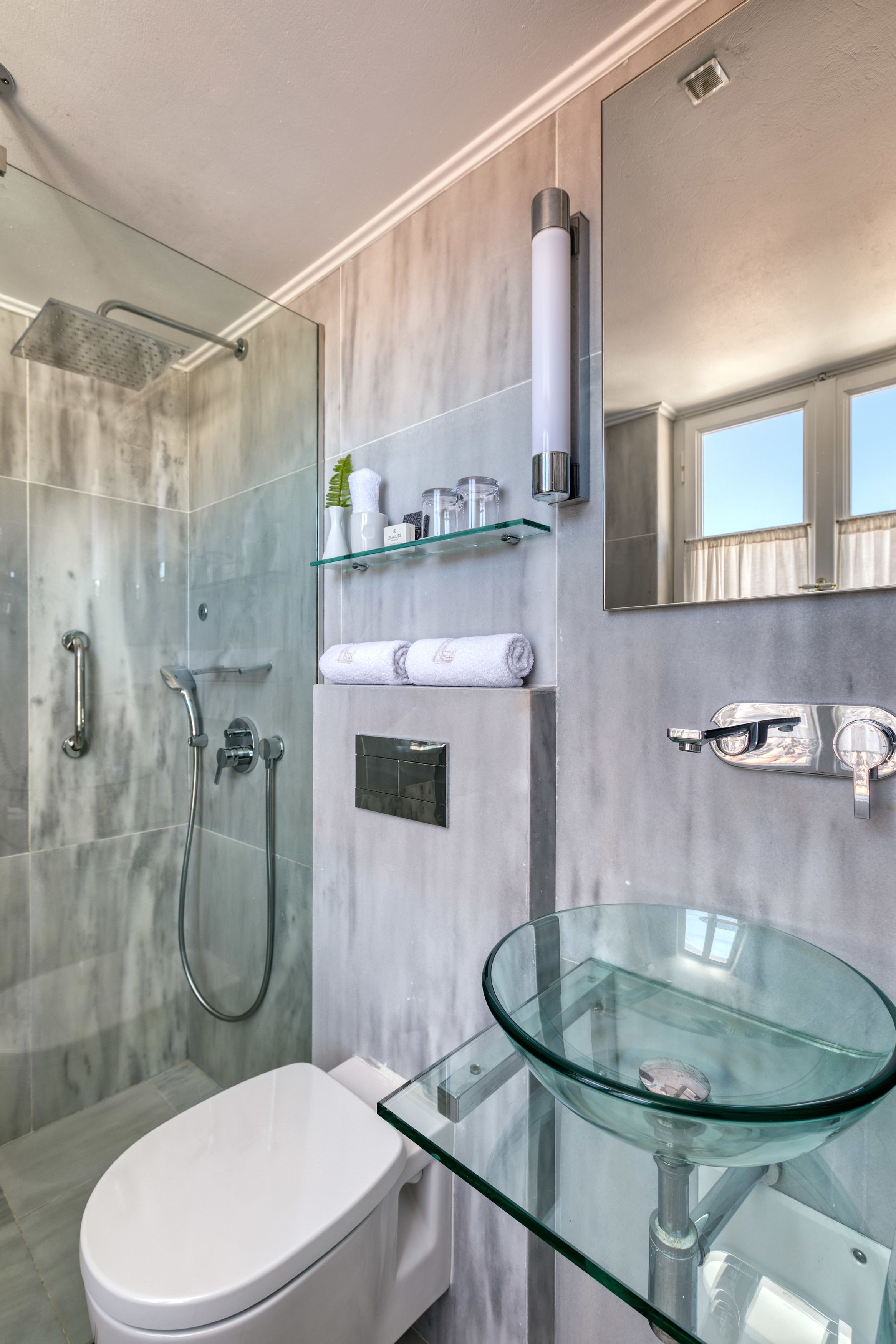 A modern bathroom with a glass sink, a glass-enclosed shower, and a marble wall.