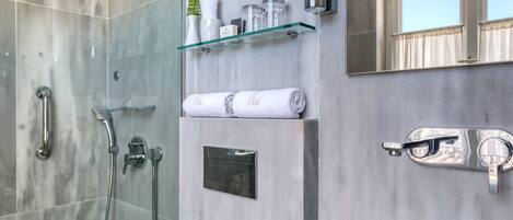 A modern bathroom with a glass sink, a glass-enclosed shower, and a marble wall.
