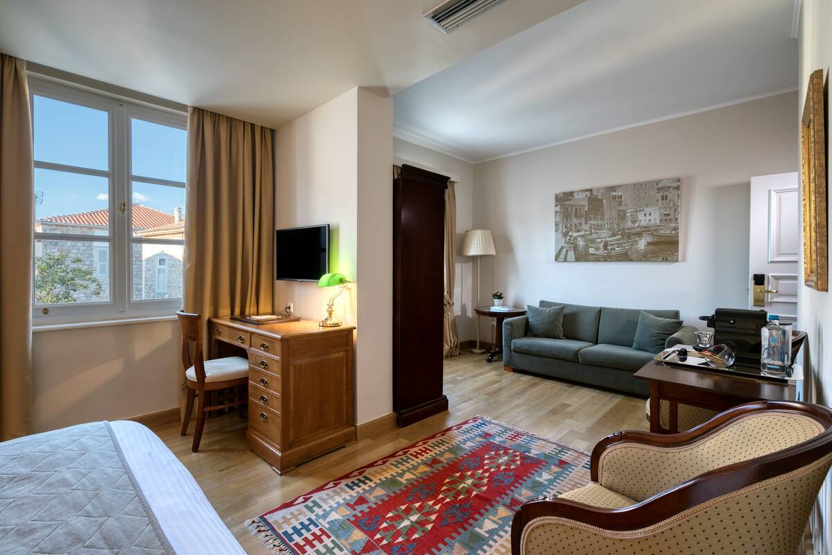 Habitación de hotel con cama, escritorio, silla, sofá y vistas al exterior.