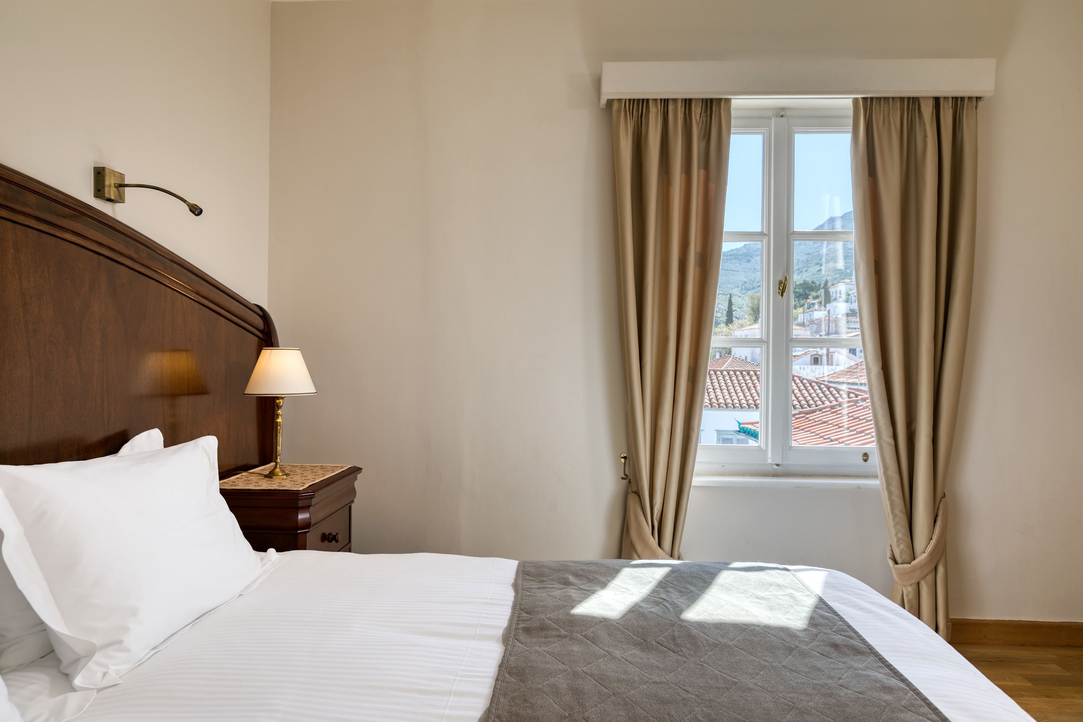 A neatly made bed with white and gray bedding, a bedside lamp, and a window with curtains.