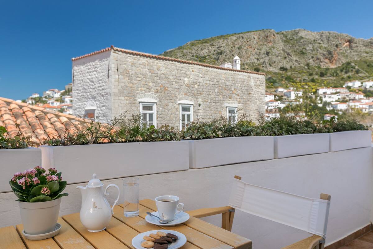 Una terraza con una mesa preparada para el té, una planta en maceta y vistas a un edificio histórico de piedra con tejado de azulejos.