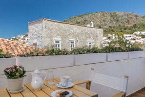 A terrace with a table set for tea, a potted plant, and a view of a historic stone building with a tiled roof.