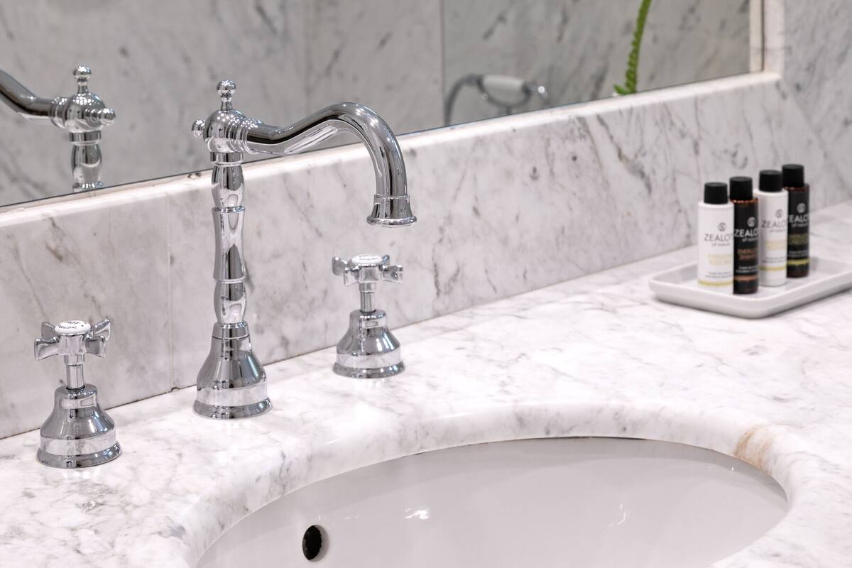 Baño con lavamanos de mármol, tres grifos y un espejo.