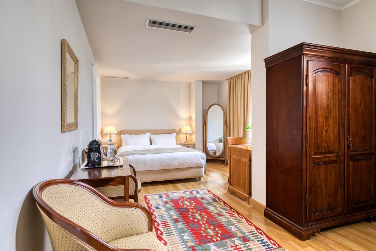 Un dormitorio con una cama, un armario de madera, una silla, una mesita de noche y una alfombra estampada.