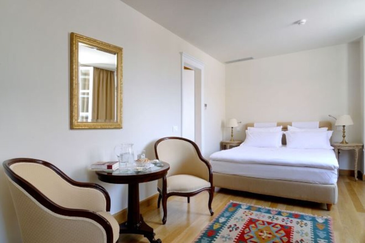A hotel room with a bed, two chairs, a small table, a mirror, and a patterned rug.