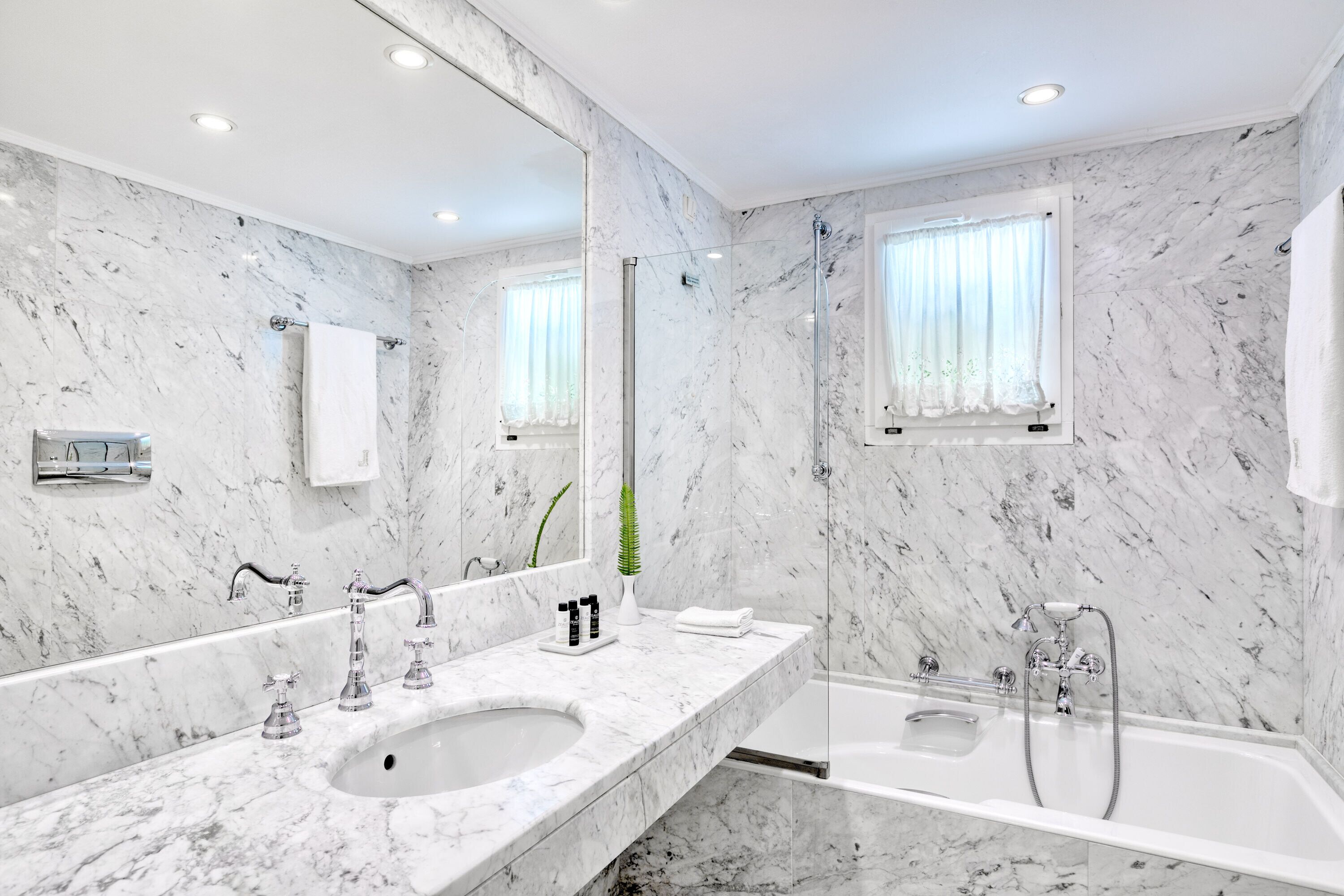 A modern bathroom with a marble sink, a large mirror, and a bathtub.