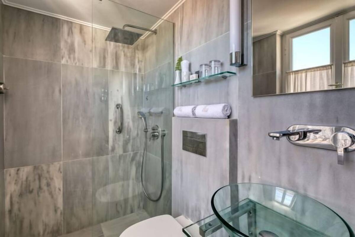 Un baño moderno con cabina de ducha de vidrio, lavamanos de vidrio y un espejo.
