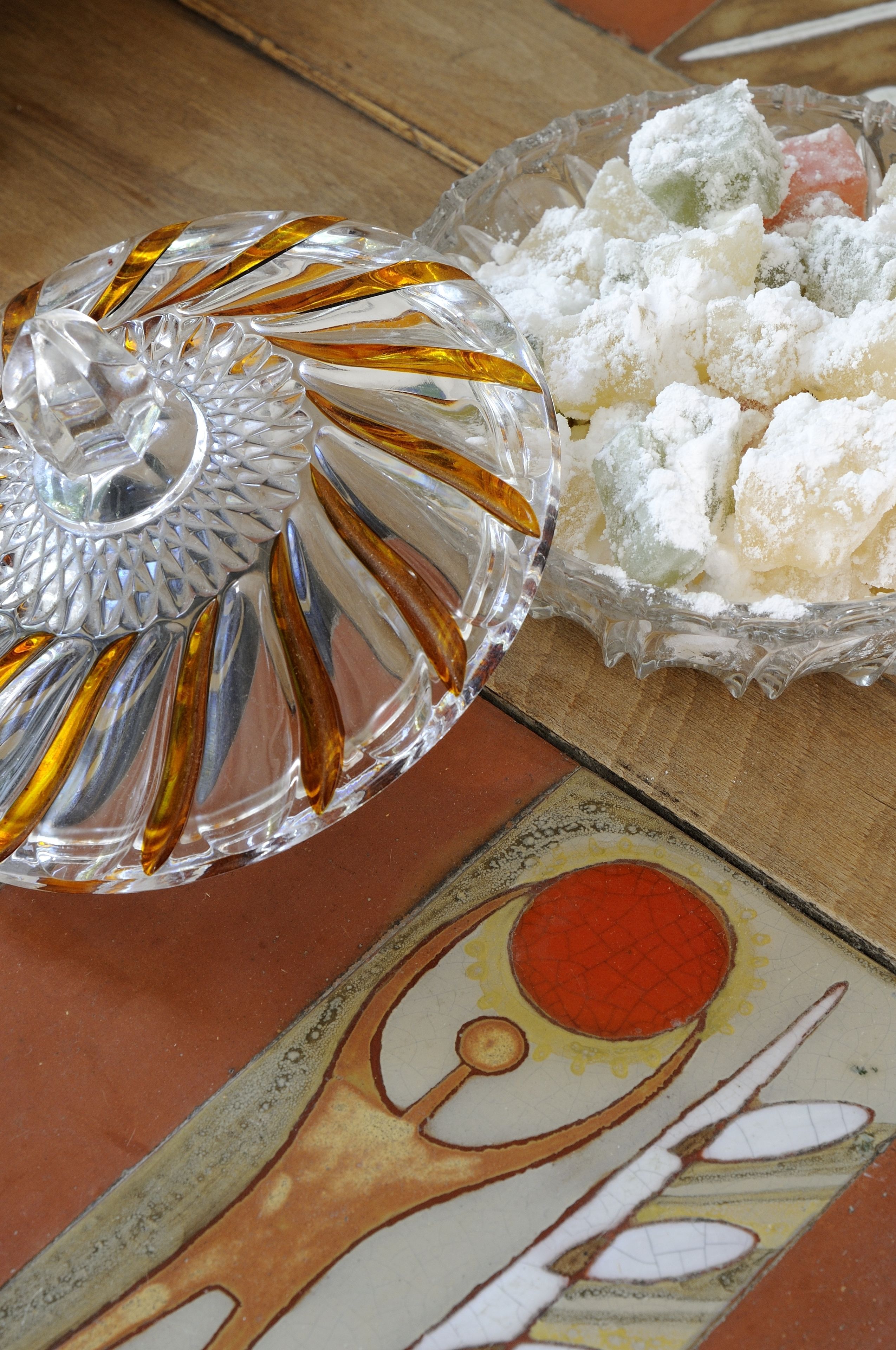 A glass dessert dish with a decorative lid and a bowl of white, powdered confections.
