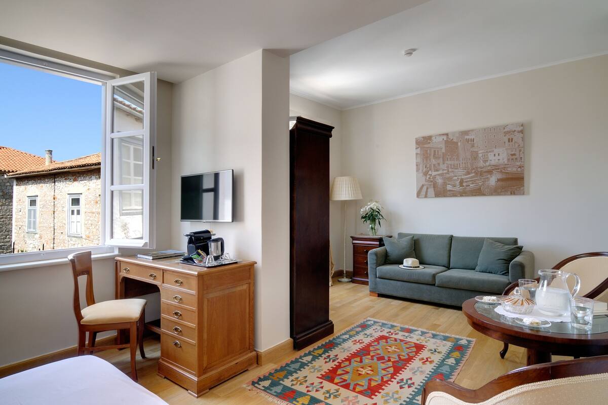 Una habitación con escritorio, silla, sofá y ventana con vistas a edificios.