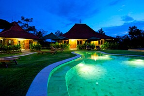 A swimming pool with a curved edge, surrounded by a lawn and picnic tables. - Three Monkeys Villas (Pecatu)