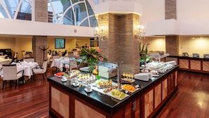 Un amplio vestíbulo de hotel con techo alto, una isla central con comida y bebidas, y vistas al cielo a través de la estructura de vidrio.