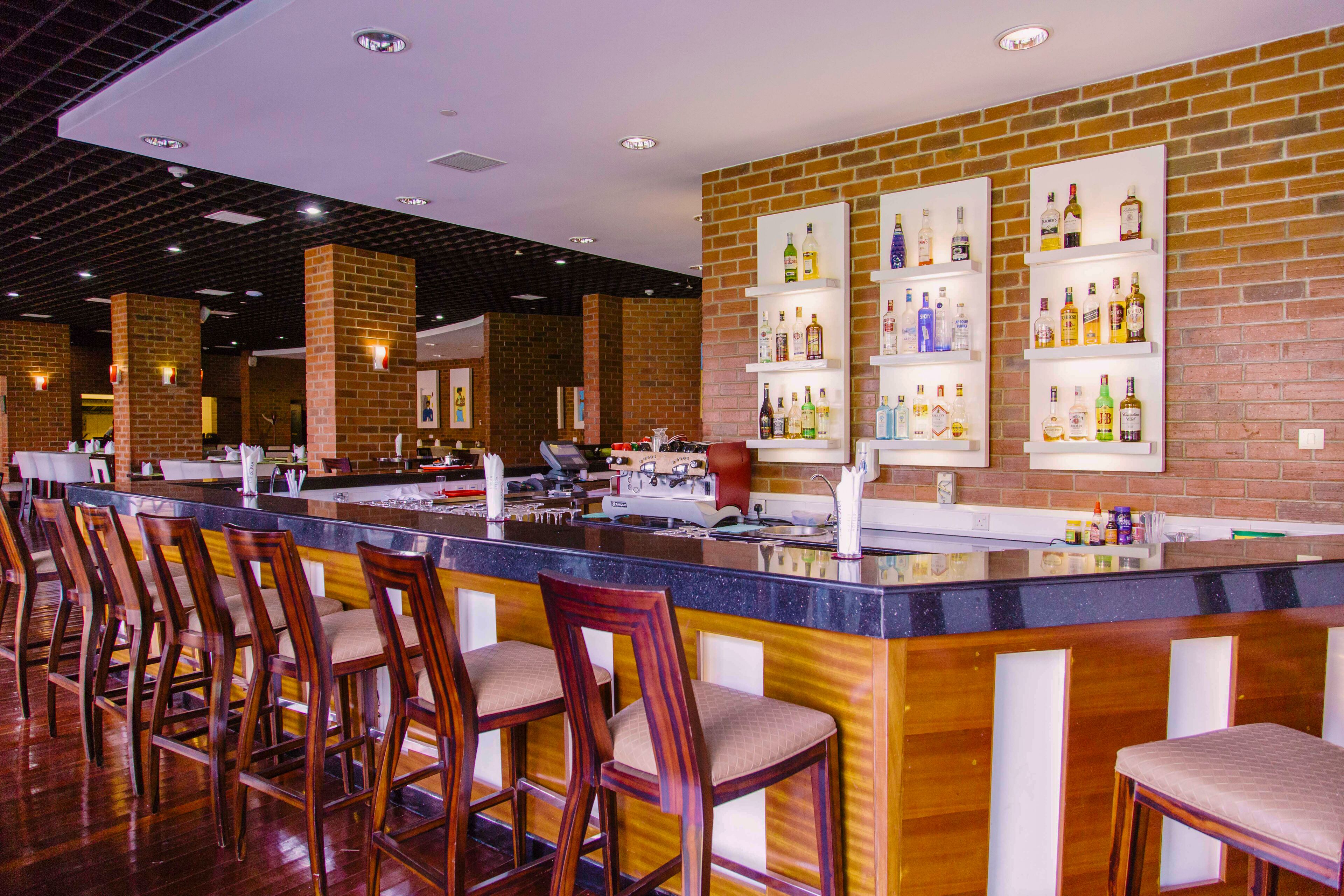 A bar area with wooden chairs, a bar counter, and shelves with bottles.