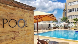 Un área de piscina con sillones de descanso, sombrillas y un cartel que dice 'POOL'.