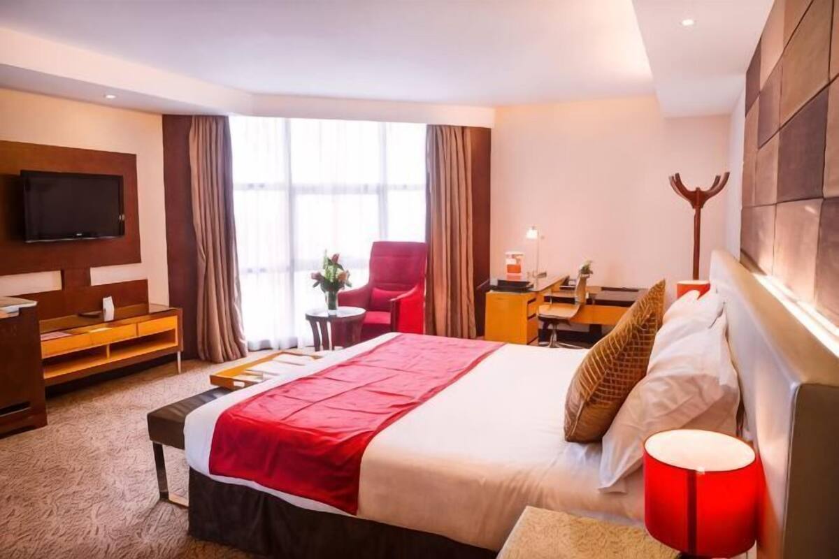 A hotel room with a bed, a TV, a desk, a chair, and a window.