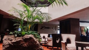 Un moderno vestíbulo de hotel con un área de descanso central, una gran escultura de roca y un techo alto con tragaluces.