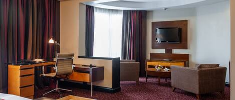 A hotel room with a bed, desk, chair, TV, and a small table with a bowl of fruit.