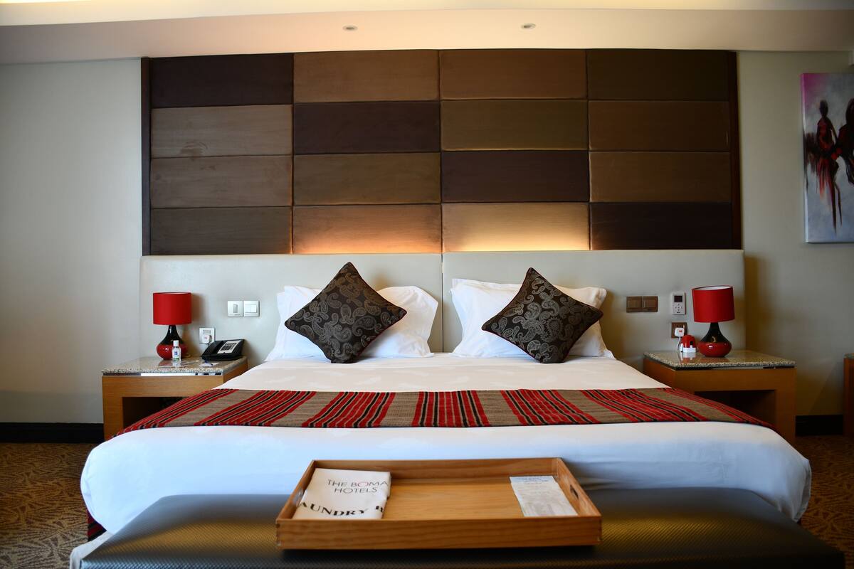 A hotel room with a large bed, two nightstands, a tray with a hotel name, and a headboard with a geometric pattern.
