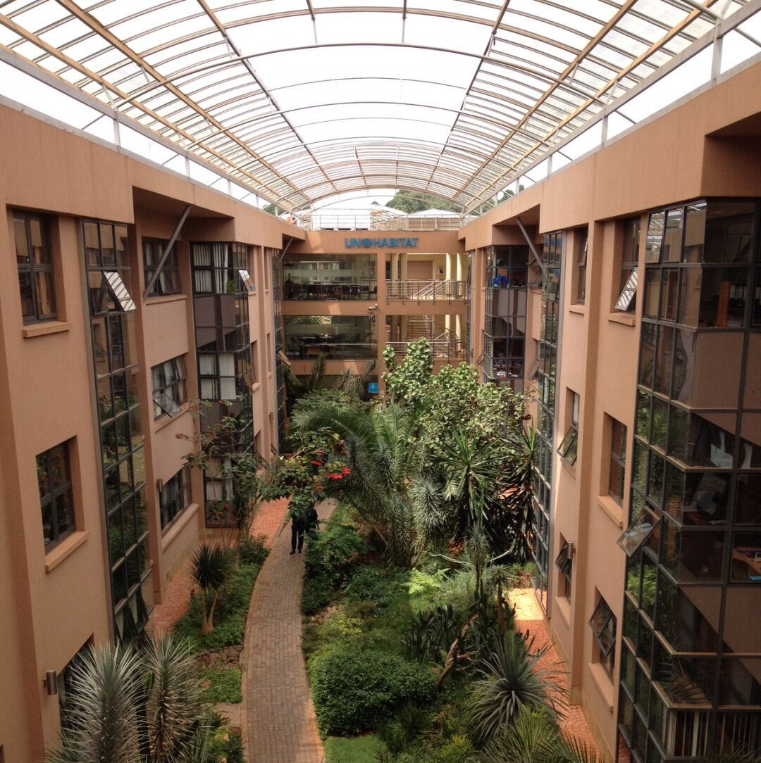 A multi-level atrium with a glass ceiling, a central garden, and a sign reading "UNIVERSITY HABITAT".
