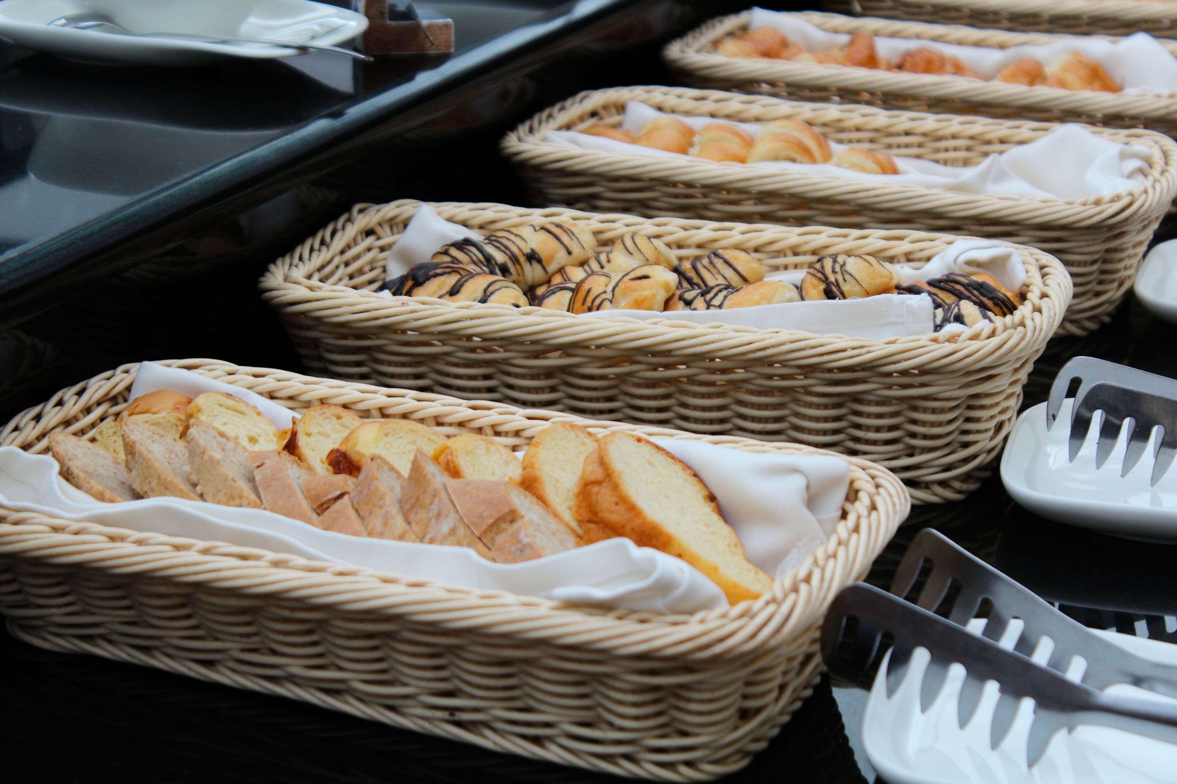 Cestas de mimbre llenas de pan y bollería sobre una mesa de buffet.