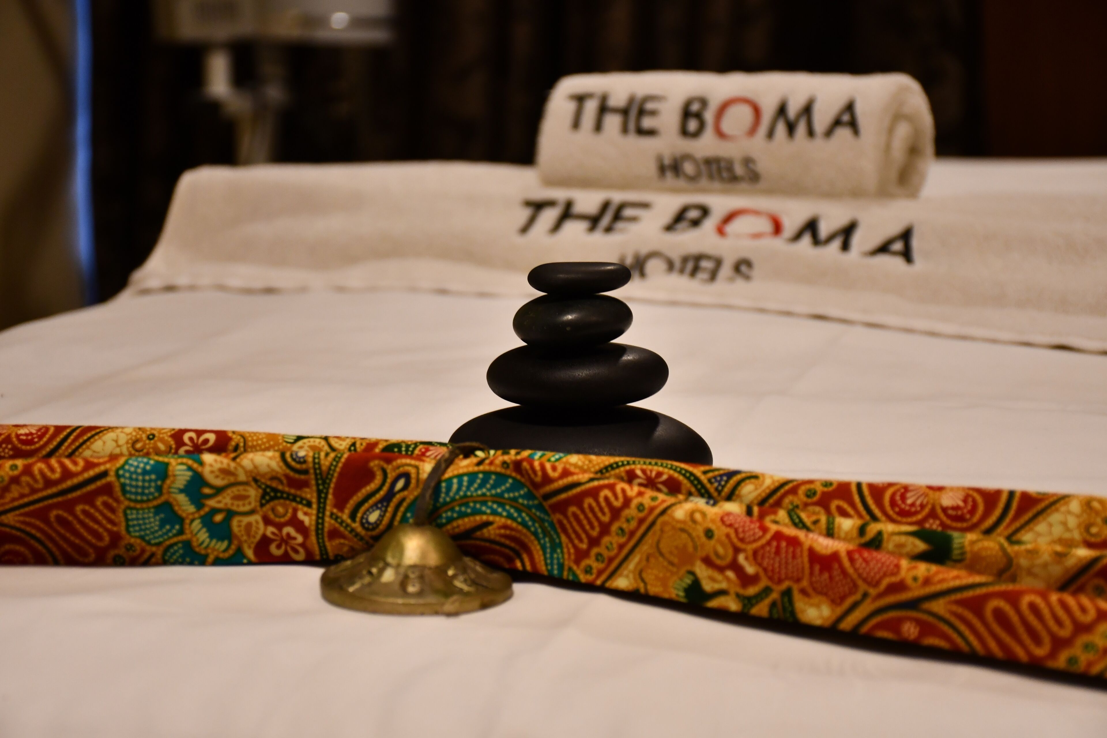 A bed with a decorative pillow, a stack of black stones, and a bell on a colorful fabric.