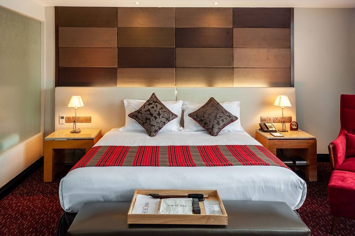 A hotel room with a large bed, two bedside tables, a red chair, and a tray with toiletries.