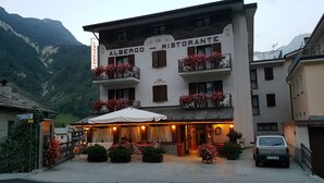 A building with balconies adorned with flowers, a sign reading "ALBERGO - RISTORANTE", and a covered outdoor seating area. - La Lanterna (Chiesa in Valmalenco)