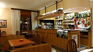 A restaurant with wooden furniture, a bar area with various bottles, and a kitchen visible through the counter. - La Lanterna (Chiesa in Valmalenco)