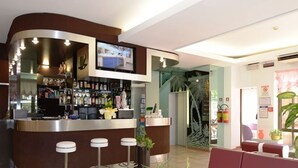 A modern bar area with a counter, stools, and a TV screen. There are seating areas with red and white furniture. - Trocadero (Riccione)