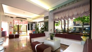 A modern hotel lobby with a seating area, a reception desk, and large windows with curtains. - Trocadero (Riccione)